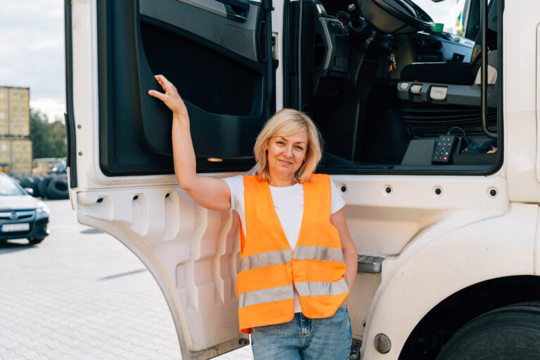Picture of a commercial truck driver wearing a reflective orange vest and standing next to her truck.