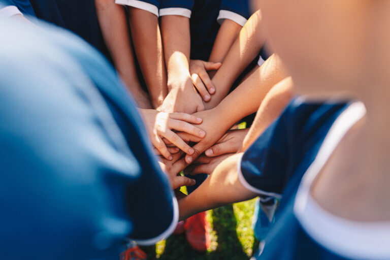 Picture of a group of children on a sports team putting their hands into the middle of a huddle.