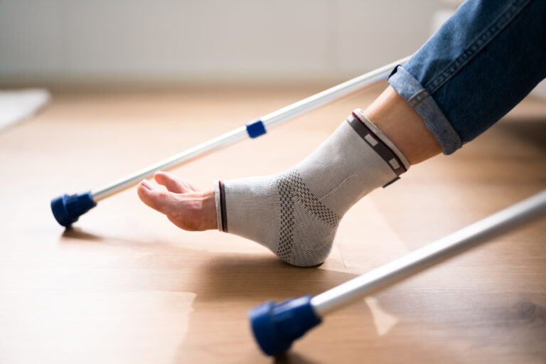 Picture of a person with a cast on their ankle sitting down, with crutches on each side of them.