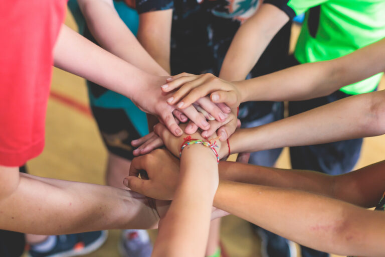 Picture of kids on a school sports team putting their hands into the middle of a huddle.