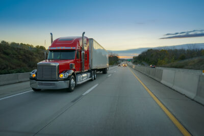 Red semi-truck on highway at sunrise