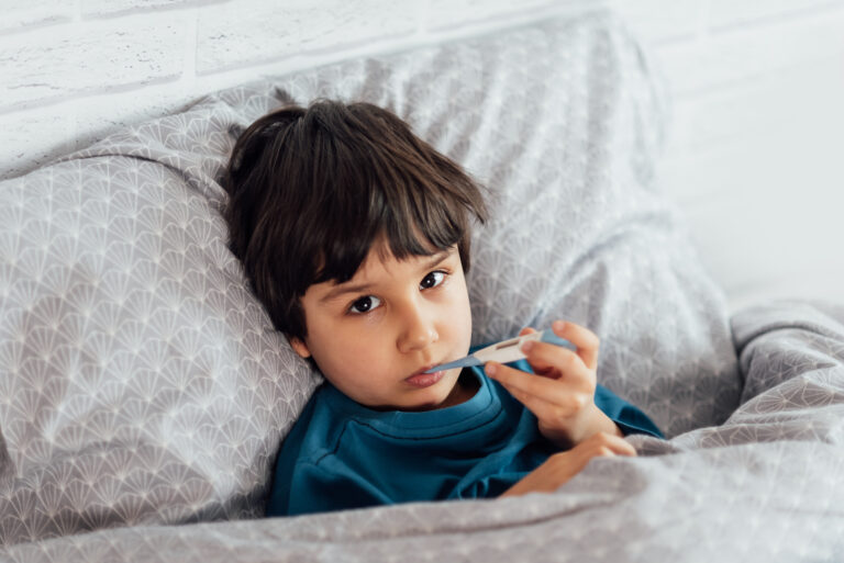 Picture of a sick child holding a thermometer and lying in bed.