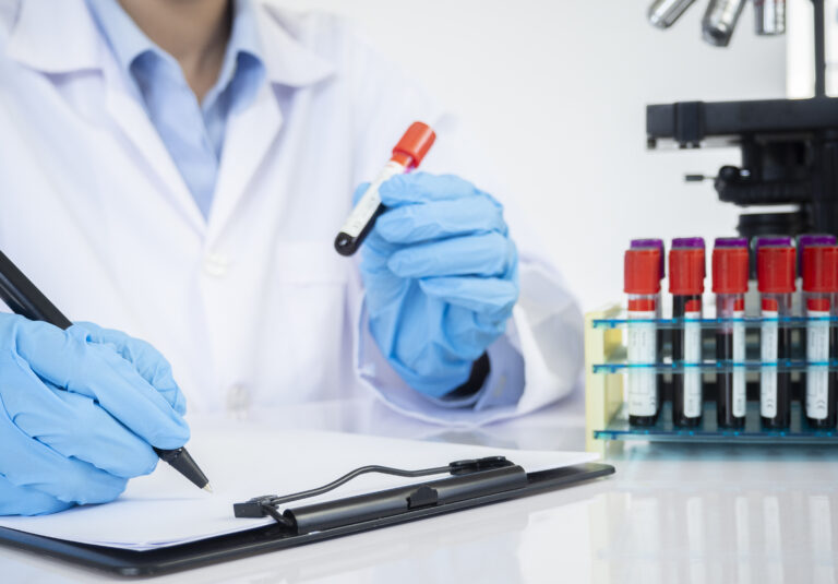 Picture of a doctor holding a test tube and writing on a clipboard.