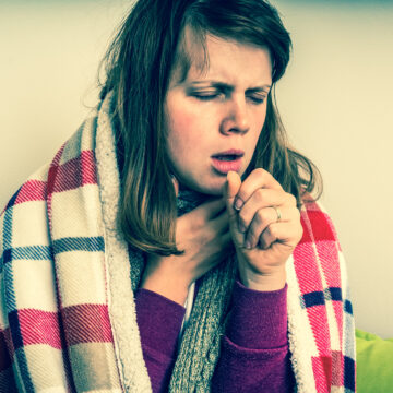 Picture of a woman with tuberculosis sitting under a blanket and coughing.