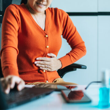 Picture of a woman with a UTI sitting at a desk and holding her abdomen in pain.