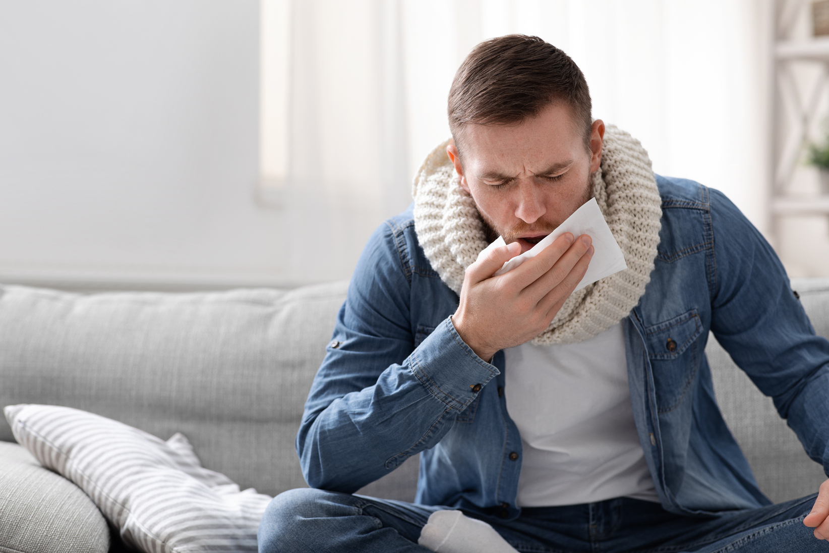 Picture of a man sitting on a couch and coughing because he has tuberculosis.