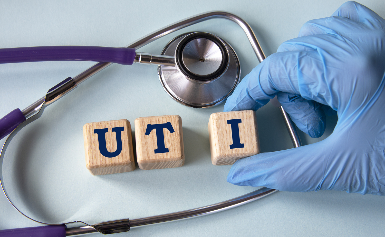 Picture of a person in a medical glove arranging wooden blocks spelling out "UTI" next to a stethoscope.