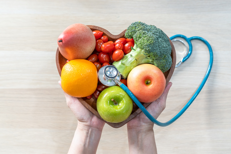 Picture of a person holding a heart-shaped bowl of fruit with a stethoscope on top.